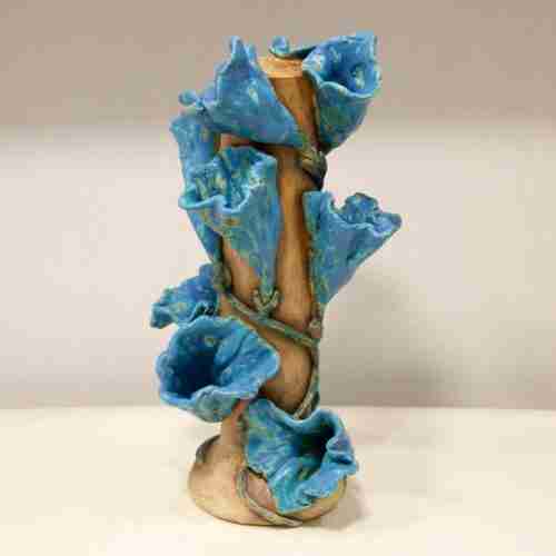 A long tall vase with blue labia flowers draped around it.