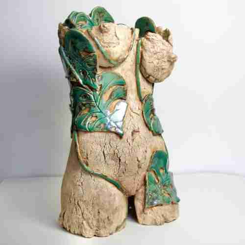 a feminine stoneware sculpture where glossy green monstera leaves entwine with a raw, cracked female torso.